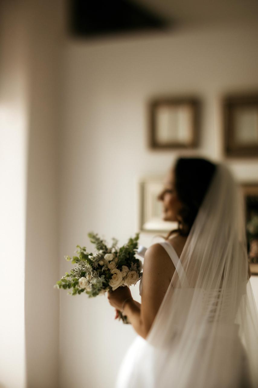 Noiva segurando bouquet de flores brancas com véu ao fundo