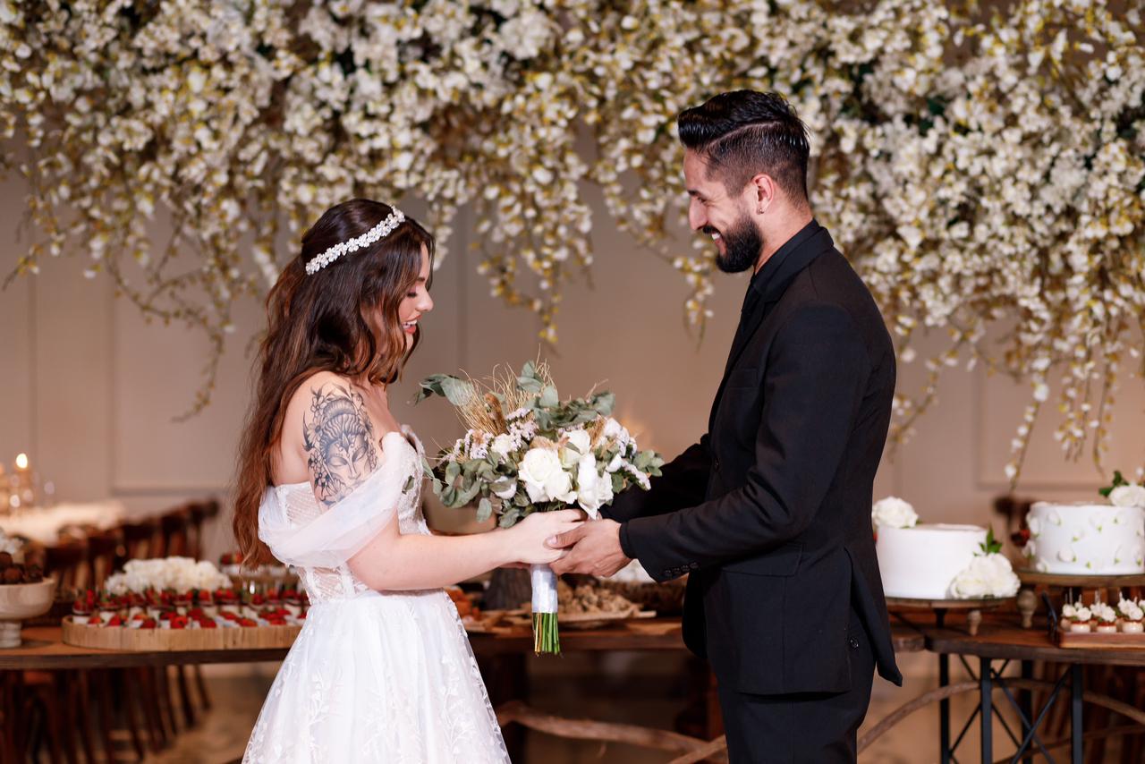 Troca de bouquet entre noivos sob arco floral branco